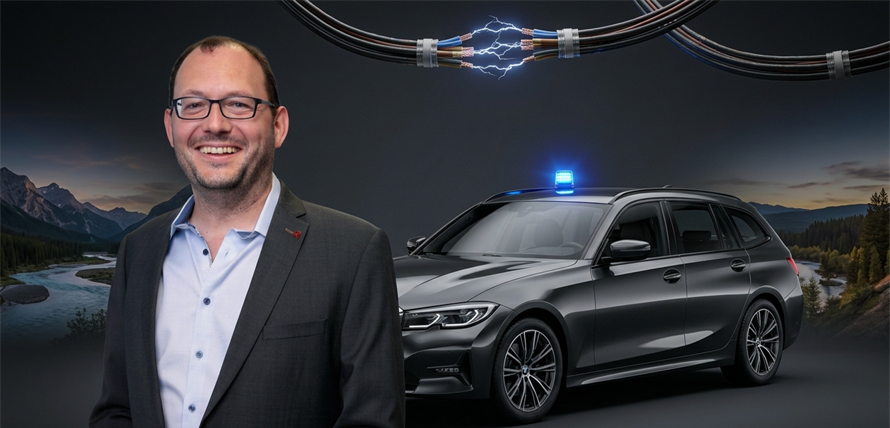 A man in a suit smiles in front of a black car with a blue light on top, set against a scenic background.